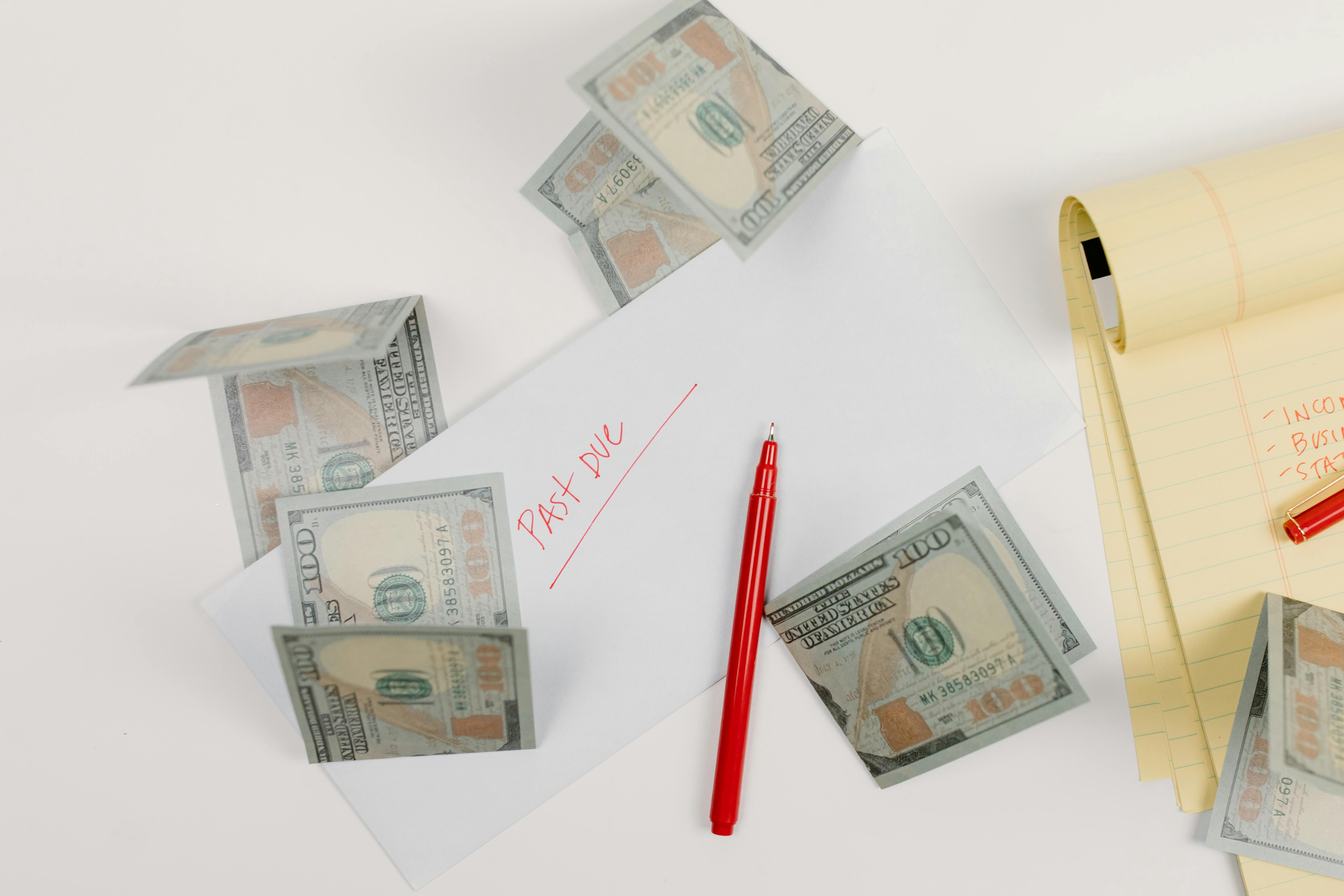 Past due envelope with dollar bills, pen, and notepad on a desk